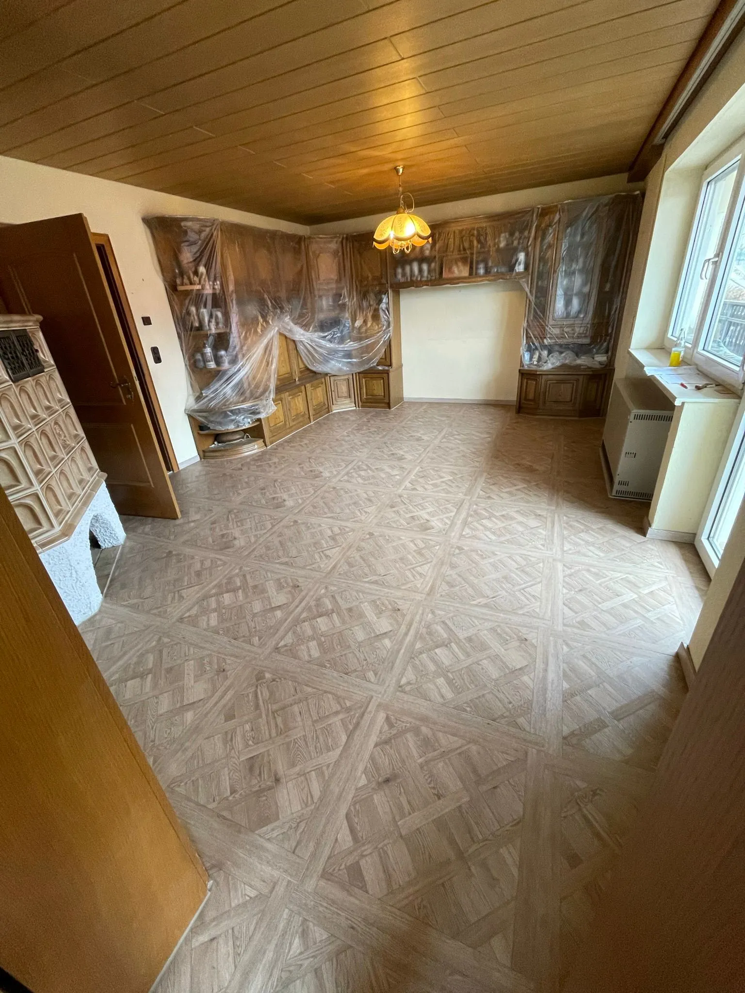 Zimmer mit Laminat im Versailles-Muster unter Holzdecke neben Kachelofen